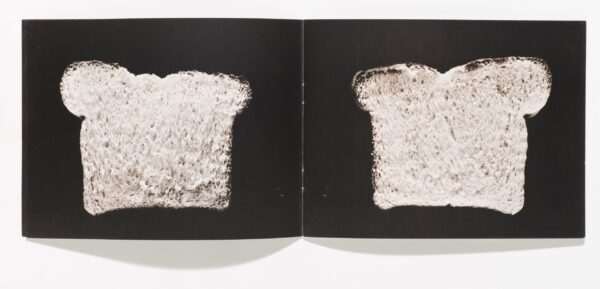 An open book featuring a slice of bread against a black background on each page.