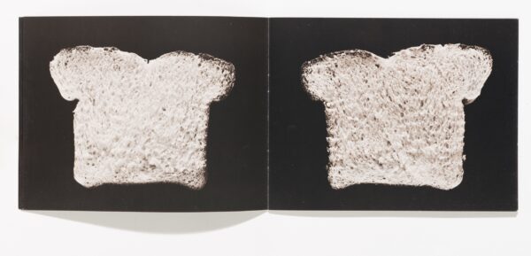 An open book featuring a slice of bread against a black background on each page.