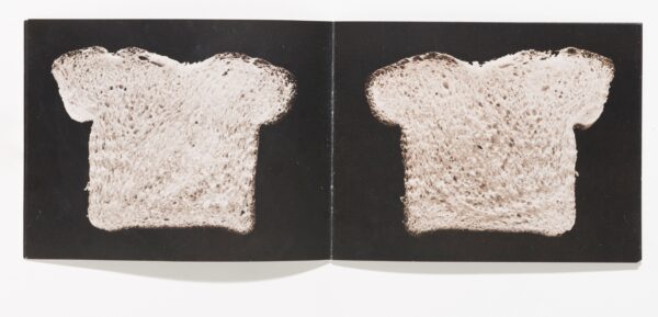 An open book featuring a slice of bread against a black background on each page.