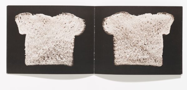 An open book featuring a slice of bread against a black background on each page.