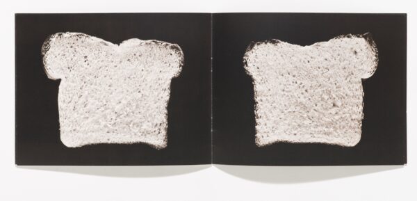 An open book featuring a slice of bread against a black background on each page.
