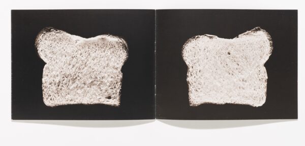 An open book featuring a slice of bread against a black background on each page.