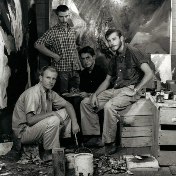 Black and white group portrait of four men with light skin sitting or standing near art-making suppleis