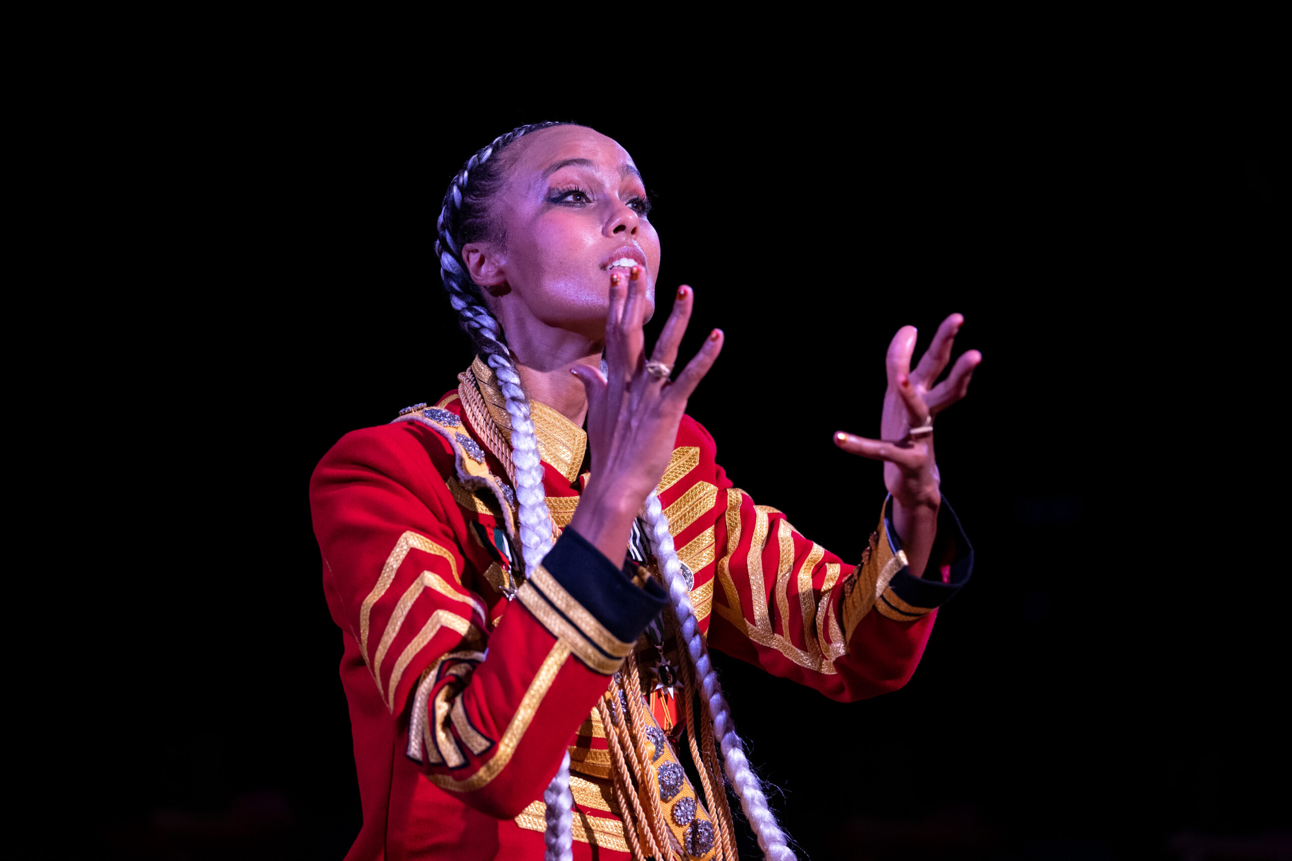 Kaneza Schaal dress in a red royal jacket gestures with both of her hands as if making a passionate argument