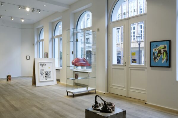 Assorted artwork on the floor and walls of a white-walled space with a row of doors and arched windows on one side