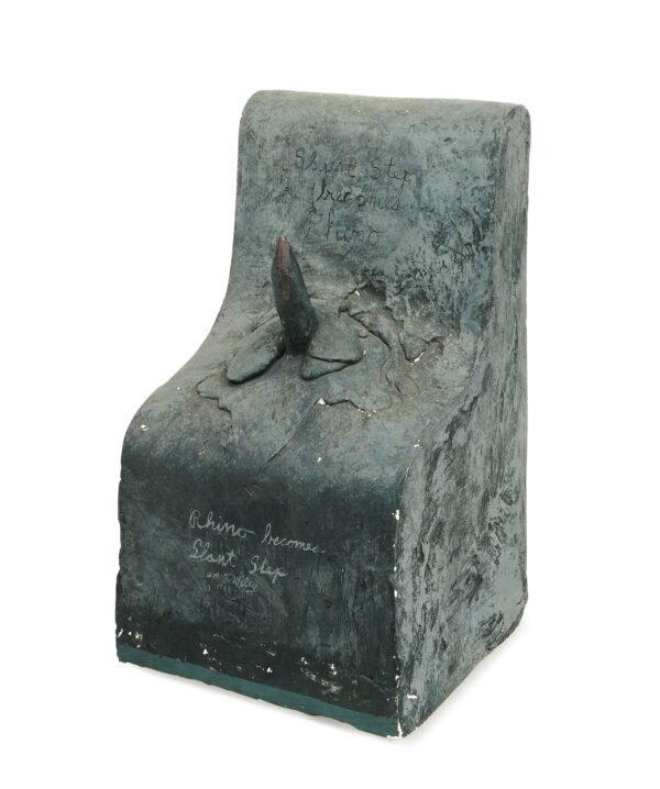 A grey slanted block that has a back support making it look like a chair. A horn made out of the same material as the chair pierces through the middle of the object.