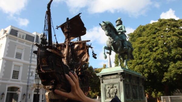 A hand holds up a ship next to an equestrian statue