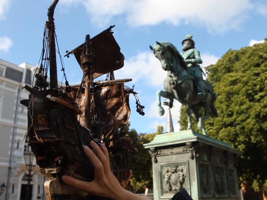 A hand holds up a ship next to an equestrian statue