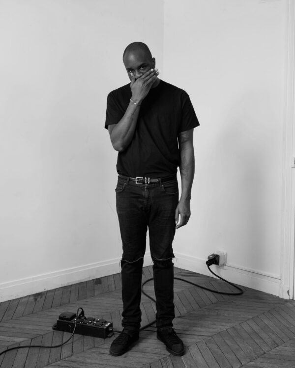 Black and white full portrait of Virgil Abloh with his right hand covering his mouth