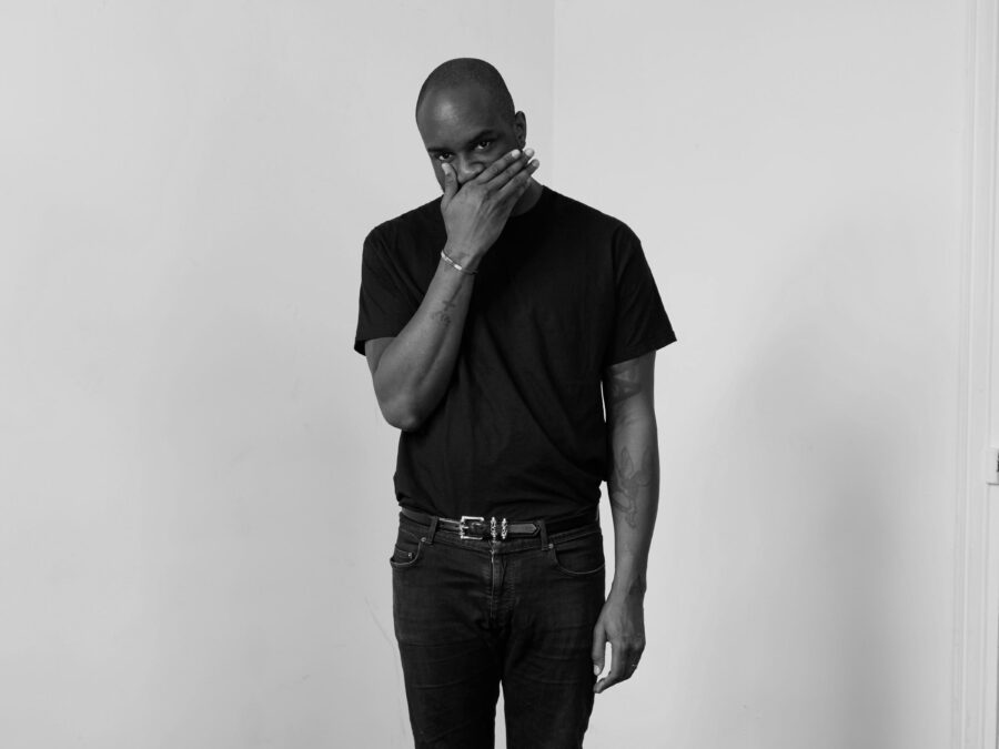 Black and white full portrait of Virgil Abloh with his right hand covering his mouth