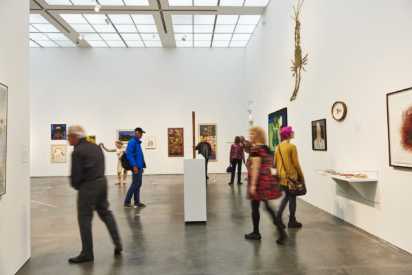 An airy white gallery filled with works of art and people who are blurred from motion.