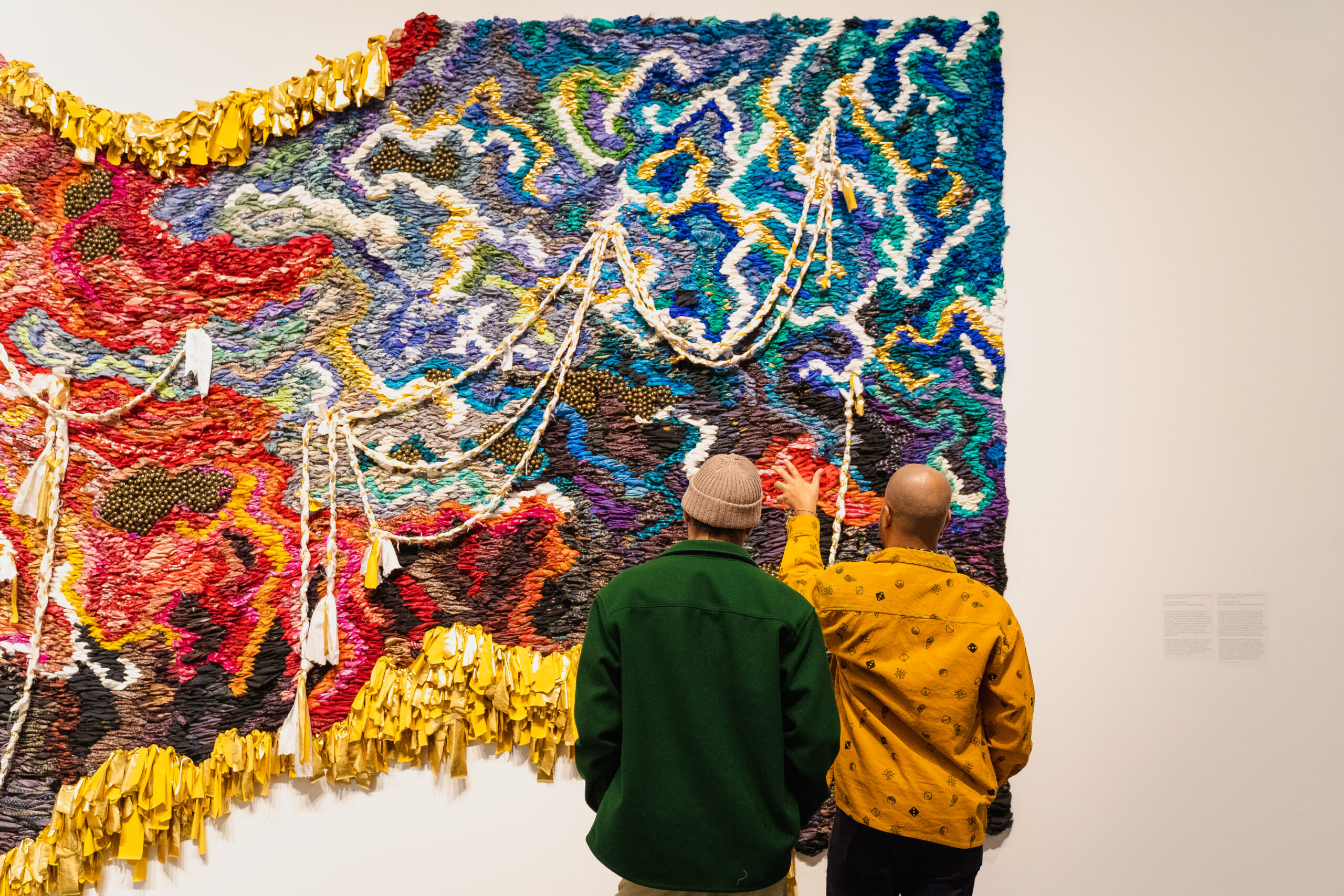 Two people looking at a large, colorful weaving hanging on the wall
