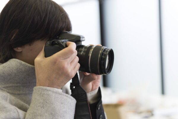 Close up of a person in a winter coat and short brown hair holding a DSLR camera up to their eye