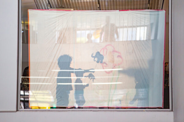 Shadows behind a white sheet of two people holding sticks with animal cutouts on them