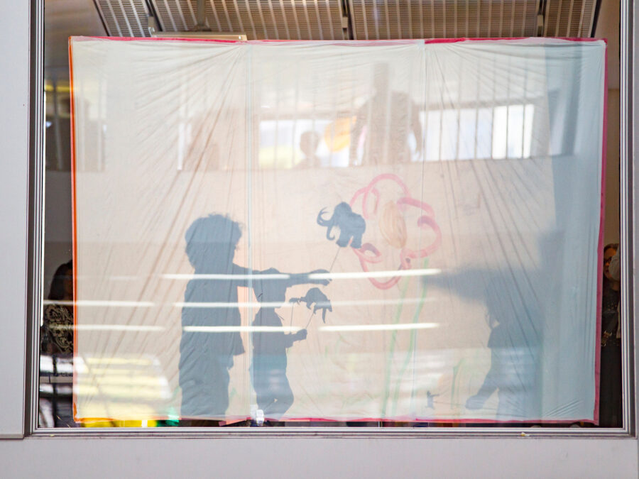 Shadows behind a white sheet of two people holding sticks with animal cutouts on them
