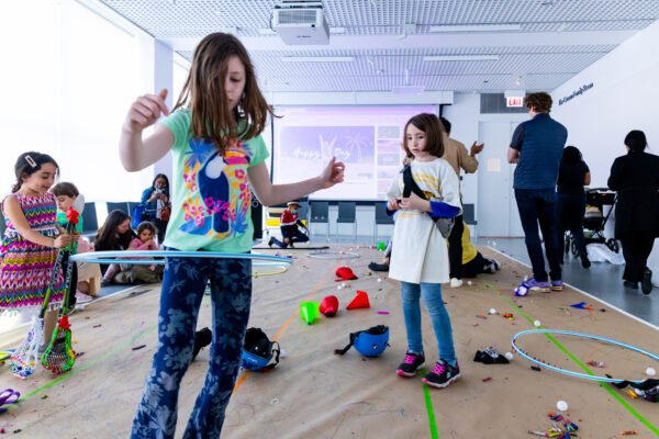 A child hula hoops while others look on in a room with brown packaging paper on the floor