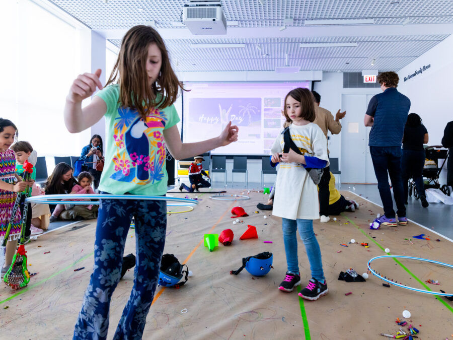 A child hula hoops while others look on in a room with brown packaging paper on the floor