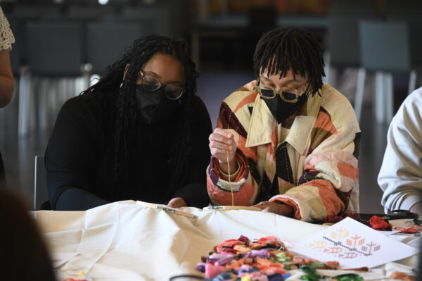 Two people wearing black masks work on a sewing project