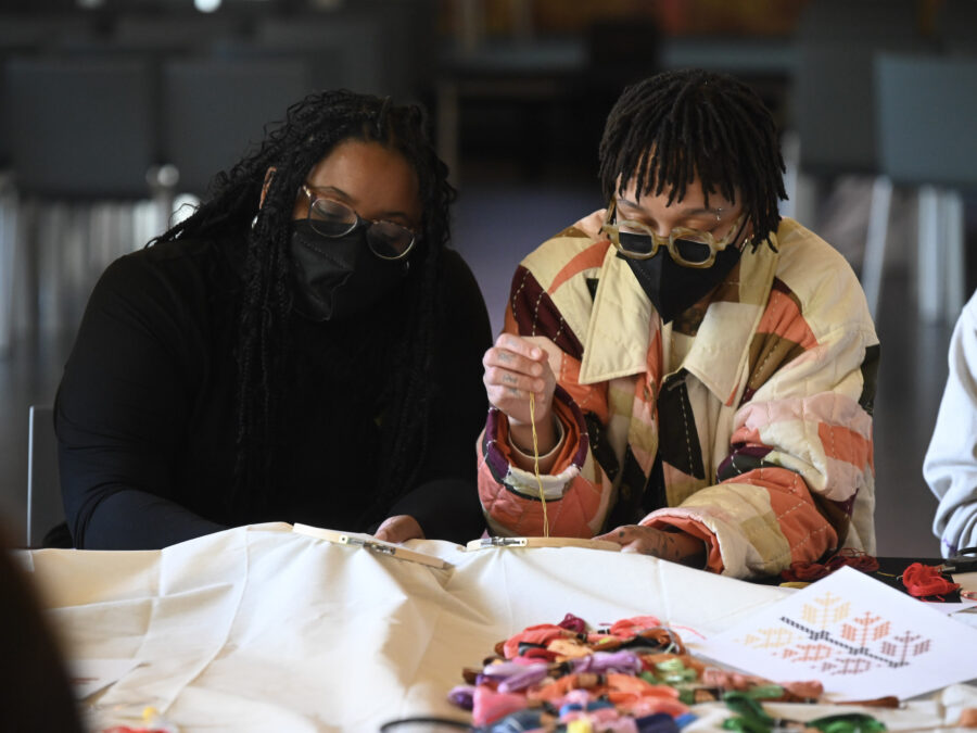 Two people wearing black masks work on a sewing project