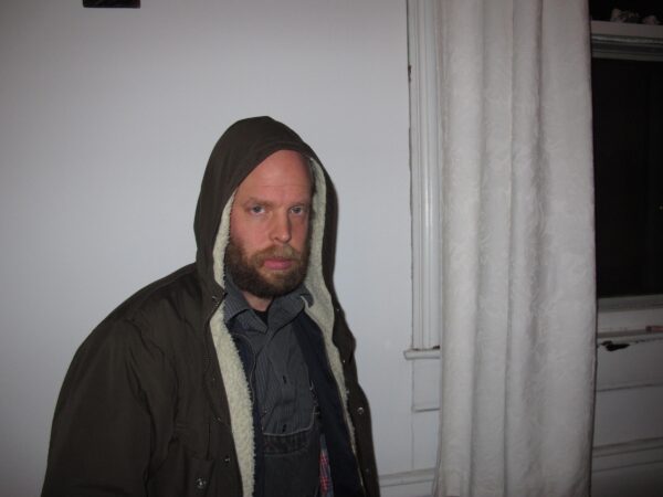 A person in a black hoodie and shirt with the hood over their head looking directly at the camera