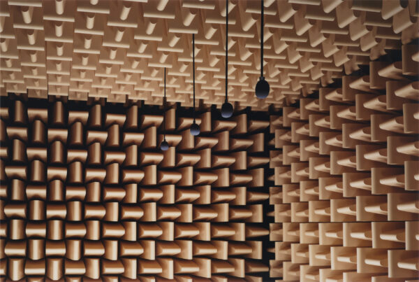 The corner of a room with brown soundproof foam on all three visible walls with four microphones hanging from the ceiling
