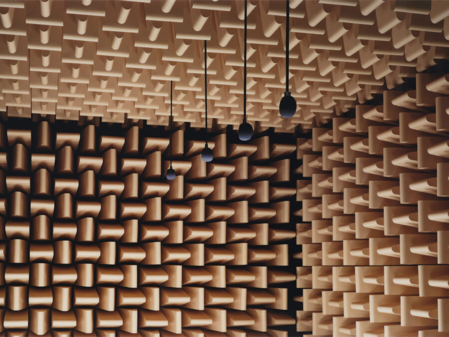 The corner of a room with brown soundproof foam on all three visible walls with four microphones hanging from the ceiling