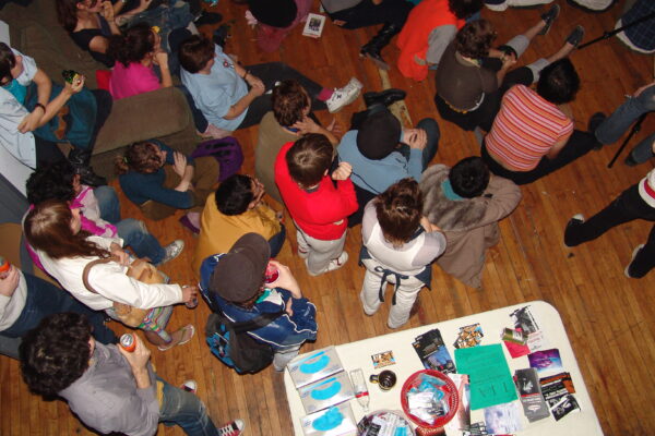 Overhead view of a group of people variously sitting or standing in a room looking at something out of view