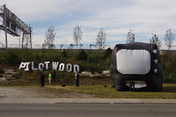 An inflatable tv near a road with blow up letters near it reading 'plotwood'