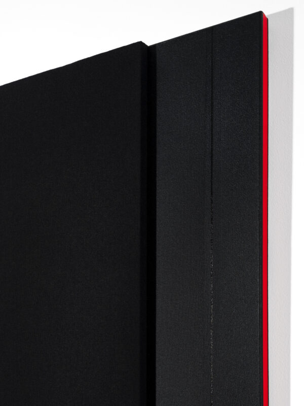 The corner of a black artwork with a red line on the edge of the otherwise black, layered canvas