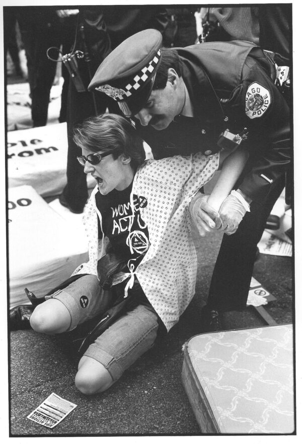 A Chicago police officer subdues a person sitting on the ground surrounded by mattresses with bold text on them