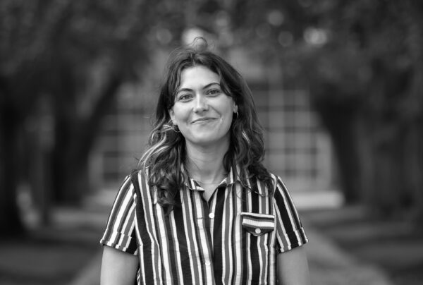 Black and white portrait of a female-presenting person wearing a striped collared shirt with wavy hair that goes just past their collarbone