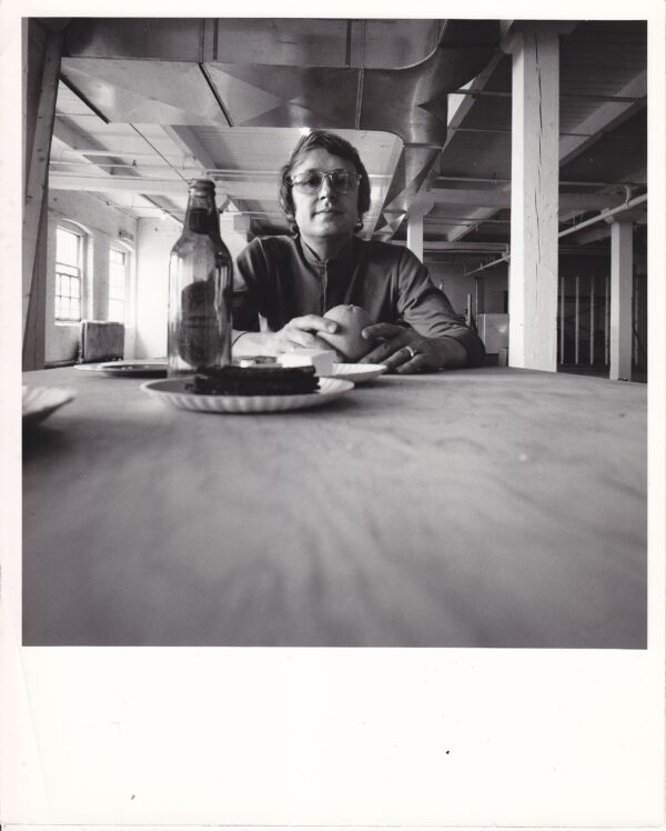 Black and white Polaroid of a man sitting at the opposite end of the table as taken from the table view.