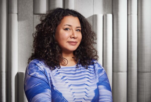 Portrait of a female-presenting person in a blue and white top with curly brown hair to their shoulders