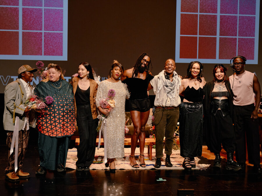 Several members of Open Television gather on a stage with two large faux windows behind them