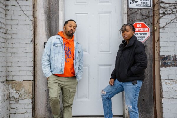 Two people stand on either side of a white exterior door dressed in cold-weather gear