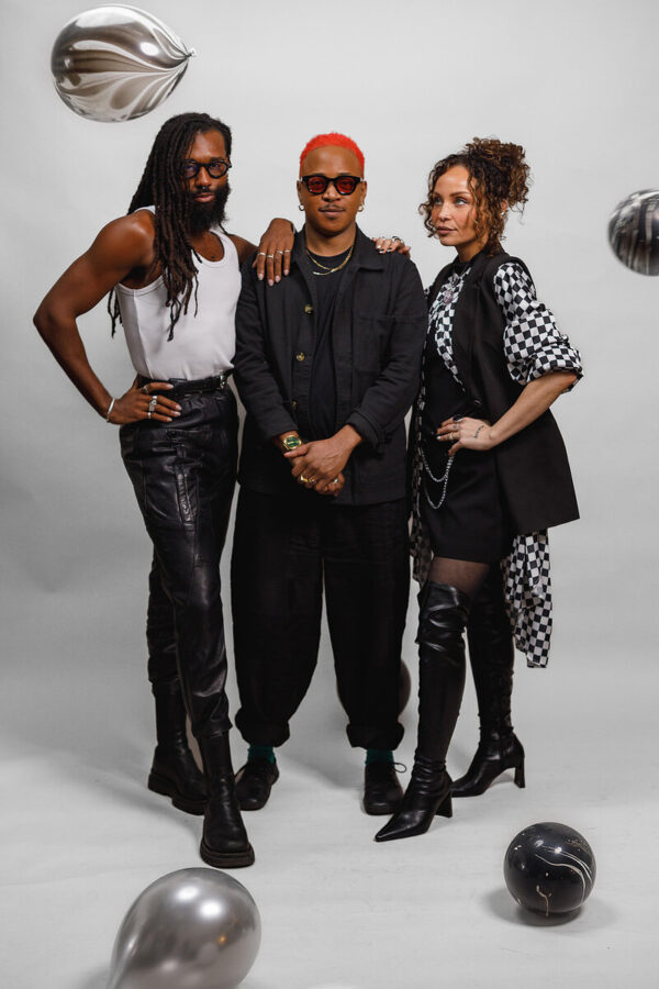 Three people with pose against a white backdrop with balloons in the air and on the ground around them