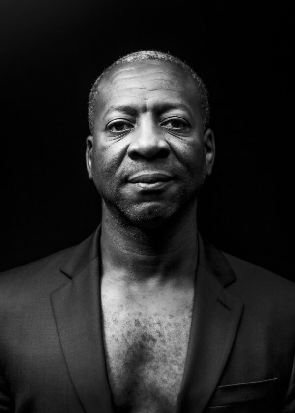 Black and white portrait of a dark-skinned male-presenting person against a black background
