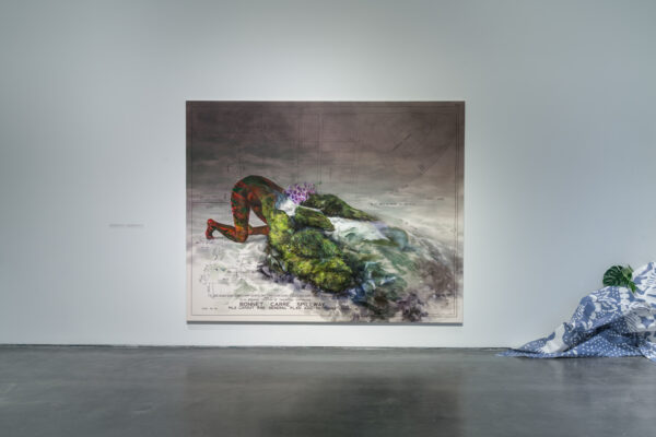 A large painting against a white wall featuring the lower half of a dark skinned body that transforms into a coastal landscape with the label Bonnet Carre Spillway. In the corner, blue and white fabric is piled on the floor