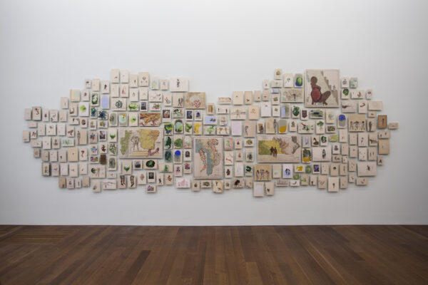 A display of multiple assorted canvas panels arranged in a cloud-like cluster on a white wall, each featuring different artistic illustrations of maps, animals, and botanical images.
