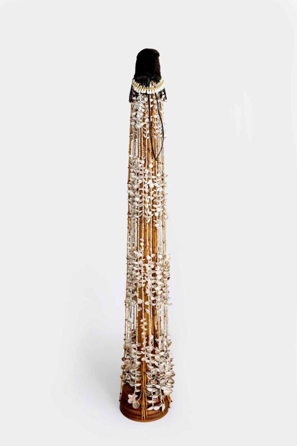 Long strands of beads and other objects encase a wooden pedestal with a black tip
