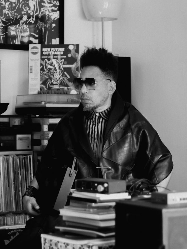 Black and white portrait of a person sitting near a stack of books wearing sunglasses and a leather jacket