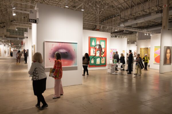 People walk through a large space divided into sections that are filled with art