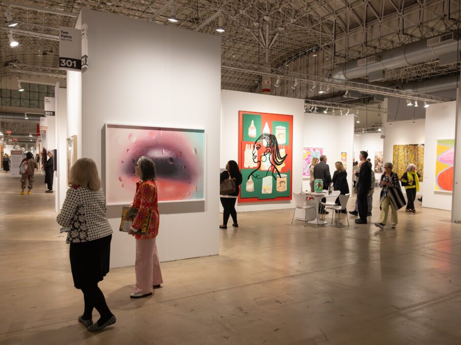 People walk through a large space divided into sections that are filled with art