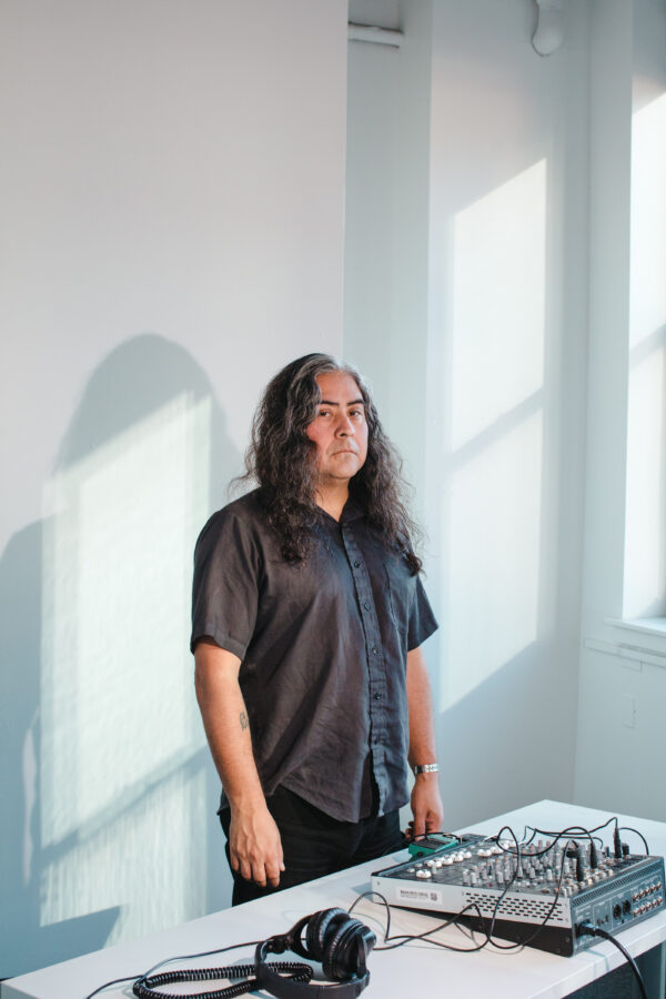 A person stands behind a table filled with sound equipment in a stark white room