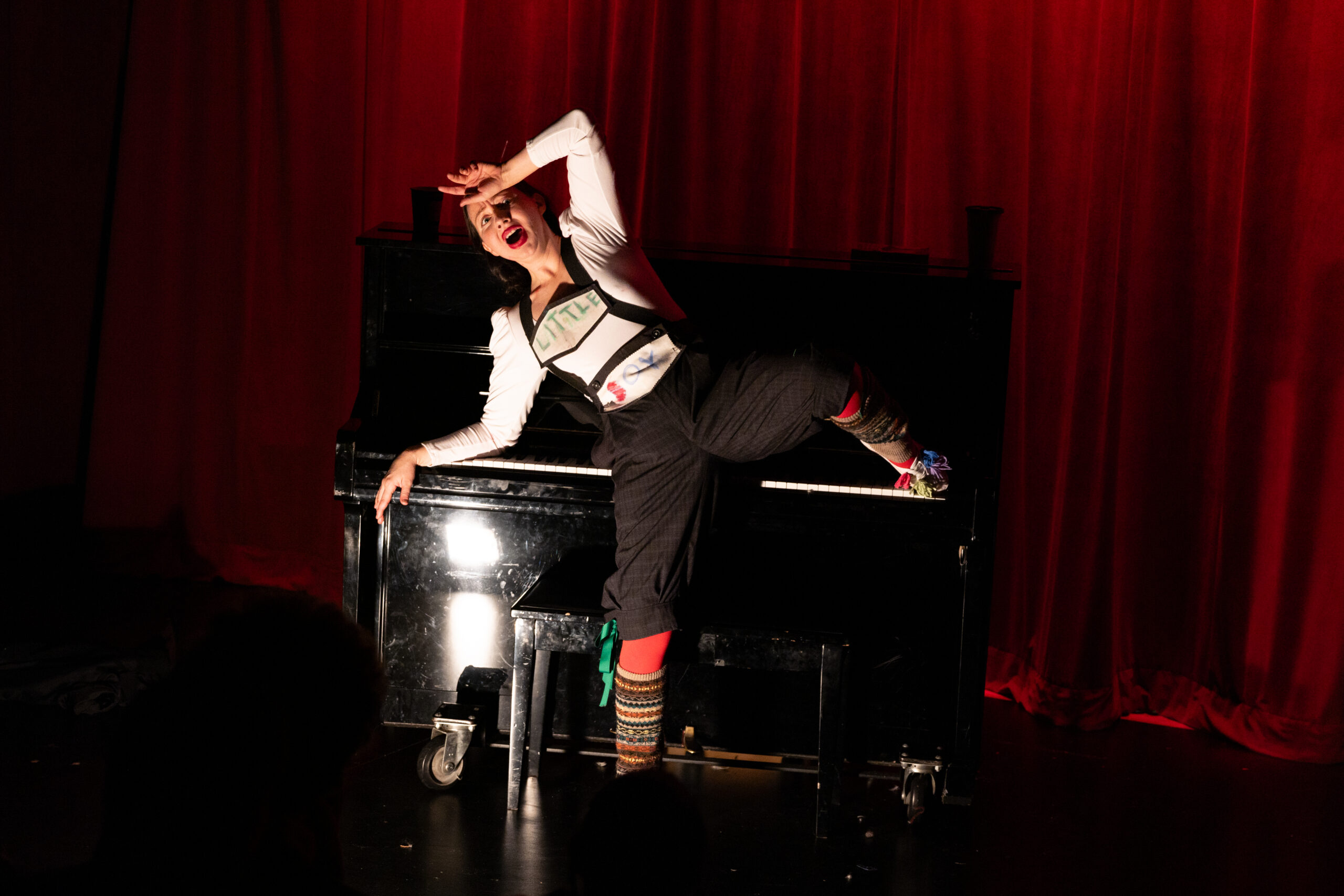 A person dressed in lederhosen with a theatrical look of anguish lays partially on an upright piano