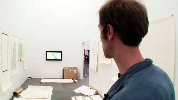 A closeup of the back of a person's head as they look at a room filled with objects on the floor and a small tv on the wall