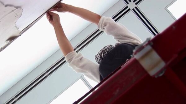 View from below as a person reaches over a railing toward a wall with artwork