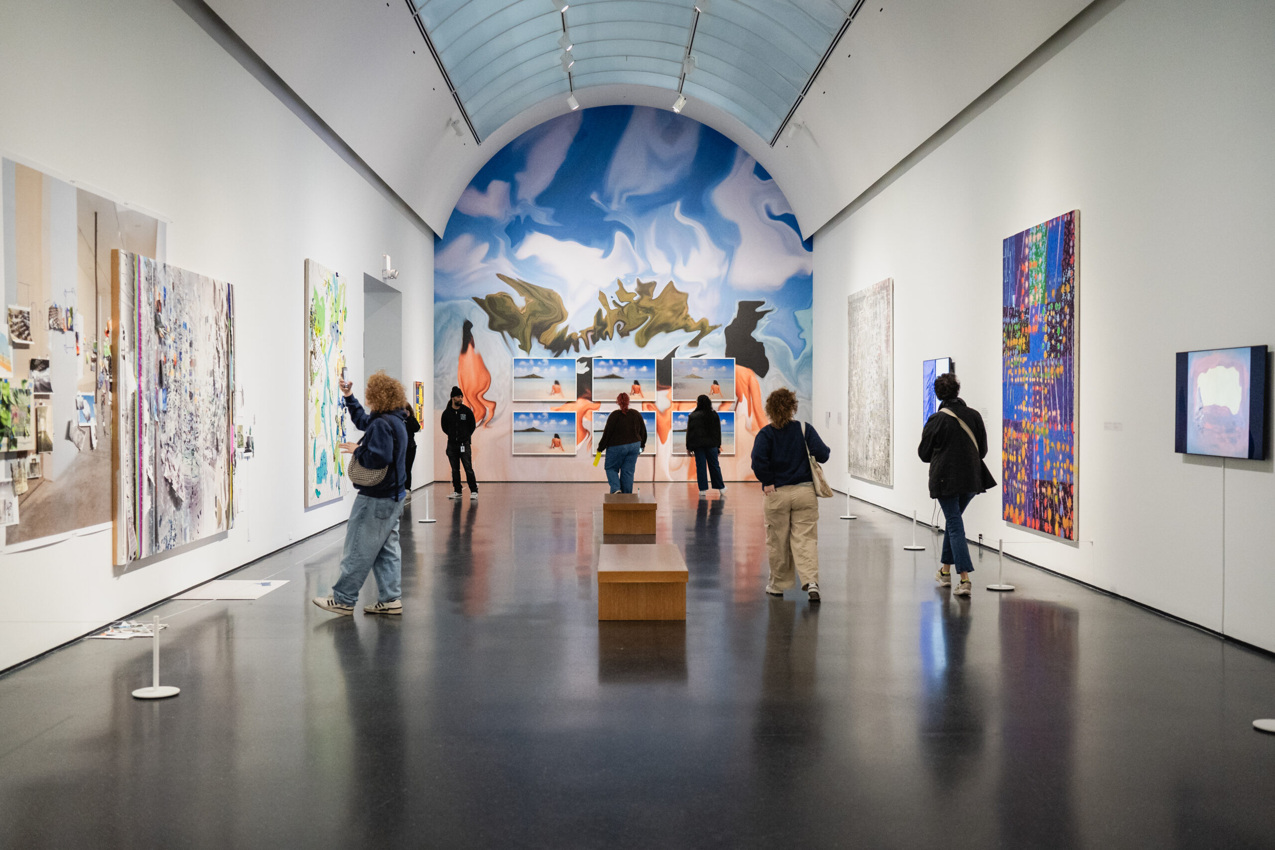 People in an arched gallery with a colorful mural at the end