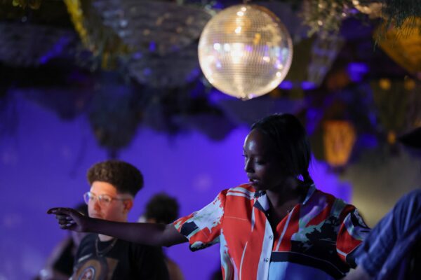 A small group of people dance under a disco ball in a dark, purple-lit room