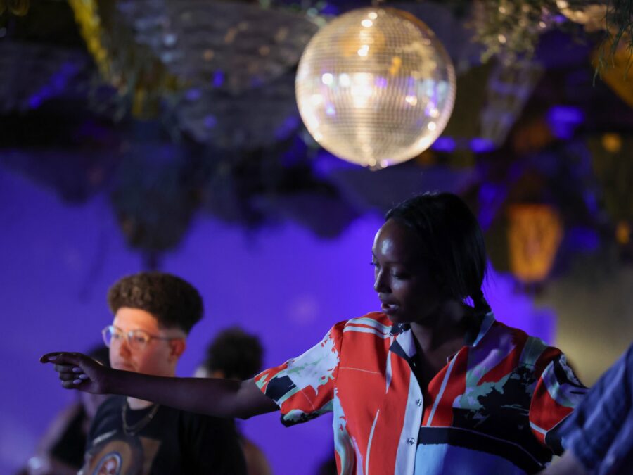 A small group of people dance under a disco ball in a dark, purple-lit room